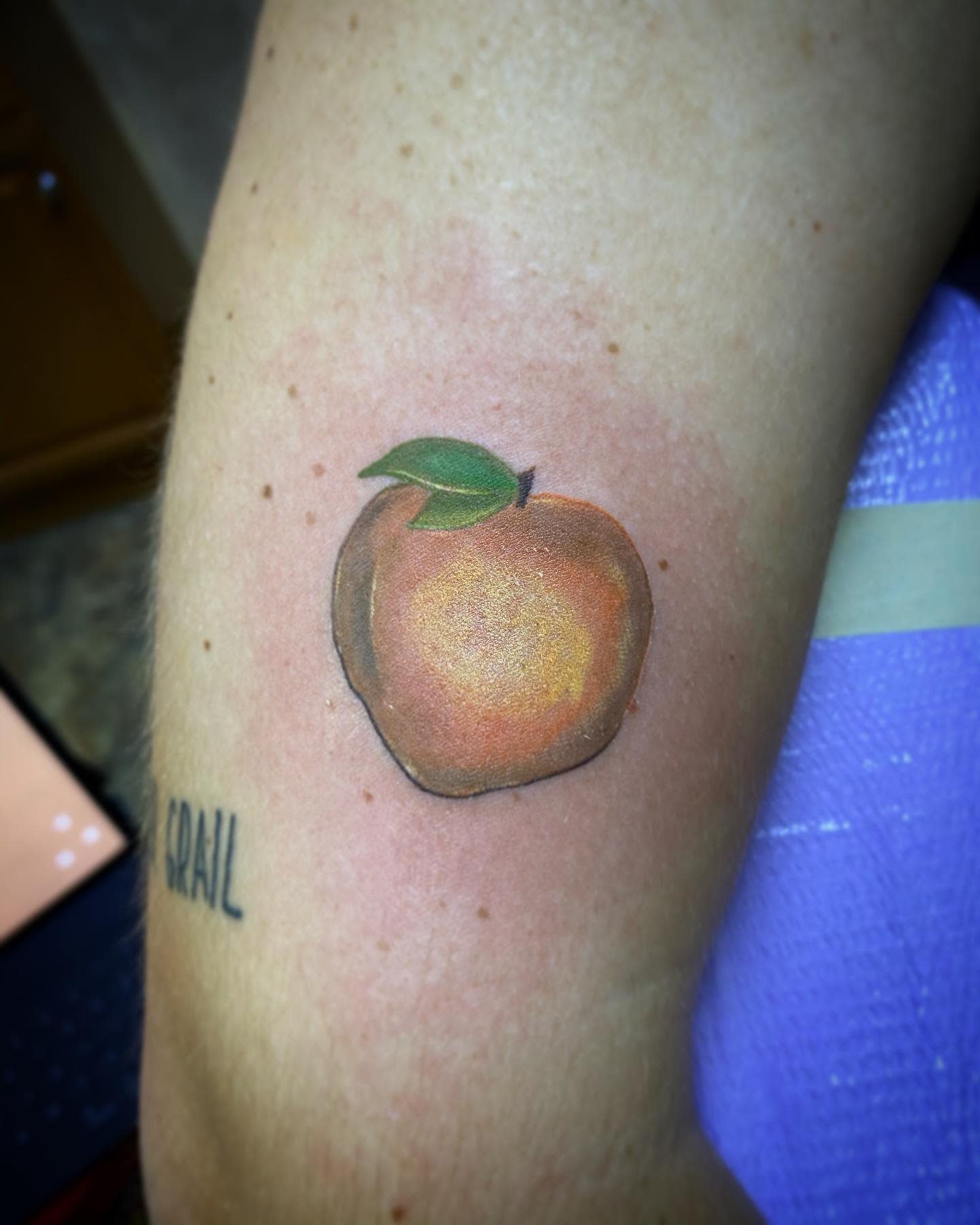 A realistic tattoo of a peach with a green leaf on an arm